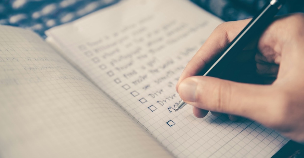 Hand met pen vinkt een takenlijst af in een notitieboek