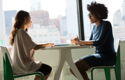 Twee vrouwen in gesprek aan een tafel bij het raam
